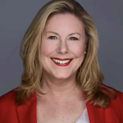 Kim Farington, studio headshot in a red blazer against a grey background.