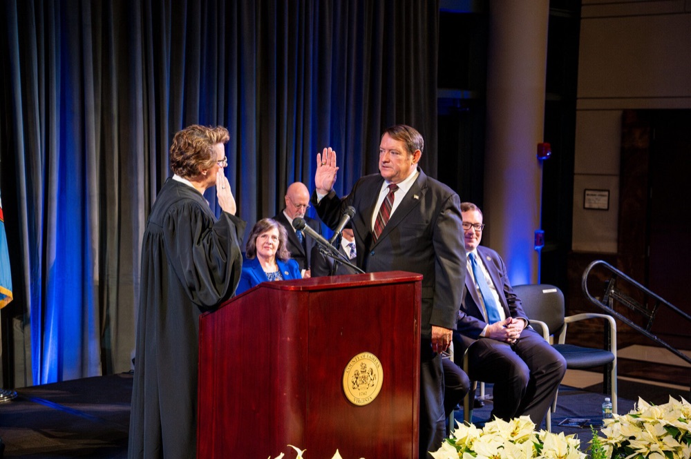 Supervisor Pat Herrity raises his right hand as a judge in black robes administers the oath of office, with officials seated behind him.